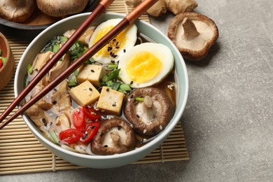 Photo of Bowl of delicious ramen and ingredients on grey table. Noodle soup