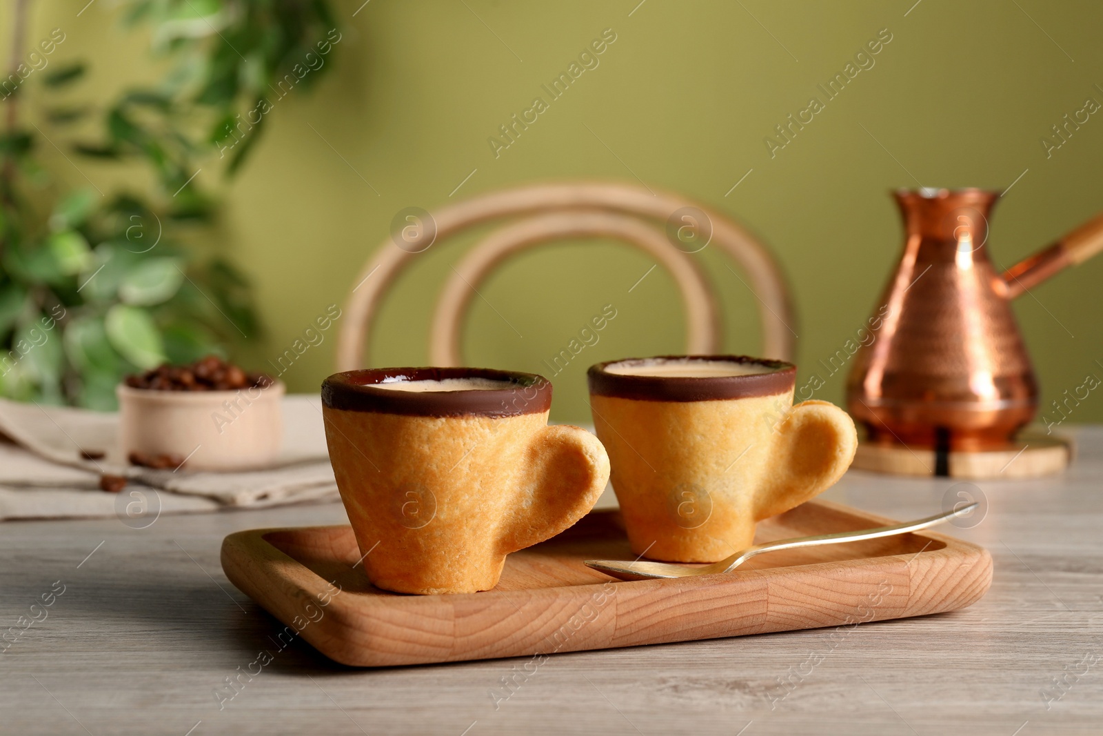 Photo of Delicious edible biscuit cups with coffee, spoon and board on wooden table