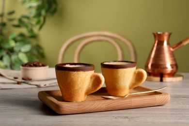 Delicious edible biscuit cups with coffee, spoon and board on wooden table