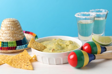 Photo of Delicious guacamole with nachos chips, Mexican sombrero hat, maracas and tequila on white wooden table