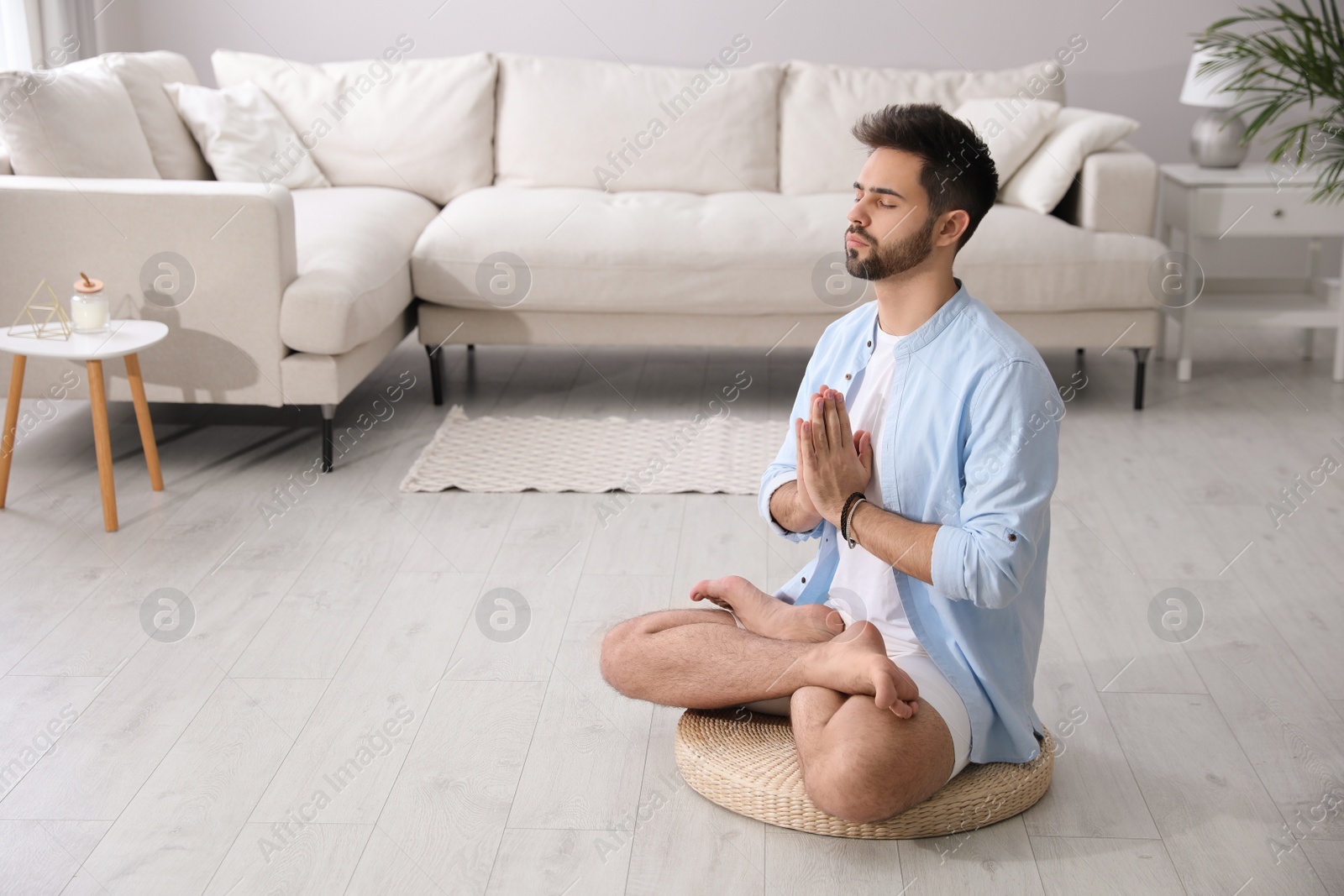 Photo of Young man meditating on straw cushion at home, space for text