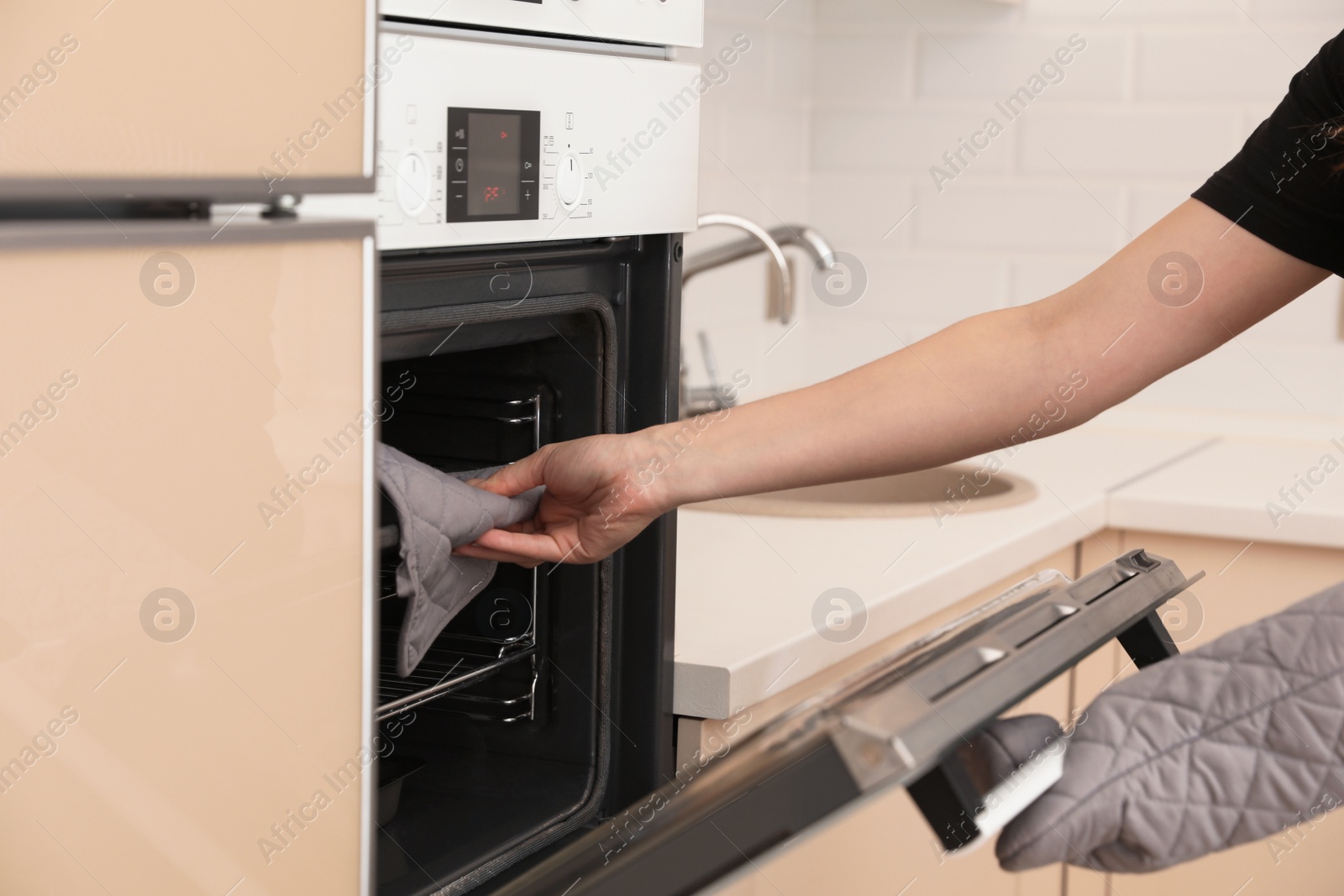 Photo of Woman putting baking tray into electric oven in kitchen, closeup