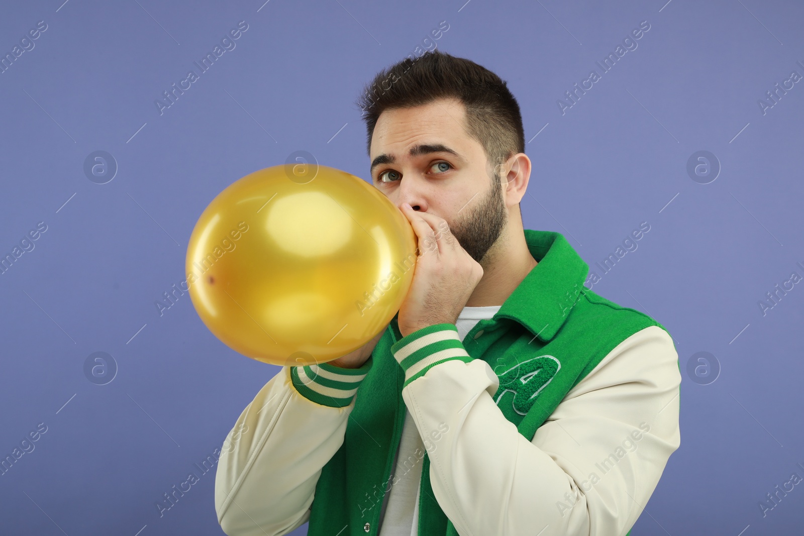 Photo of Man inflating bright balloon on violet background