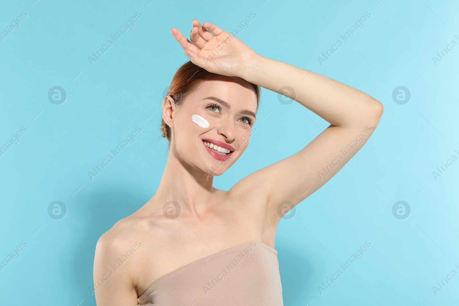 Photo of Beautiful young woman with sun protection cream on her face against light blue background