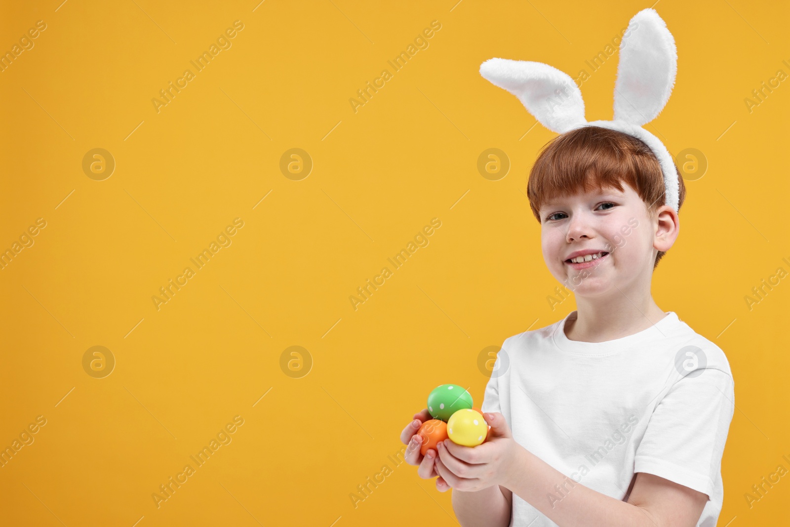 Photo of Easter celebration. Cute little boy with bunny ears and painted eggs on orange background. Space for text