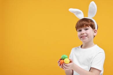 Easter celebration. Cute little boy with bunny ears and painted eggs on orange background. Space for text