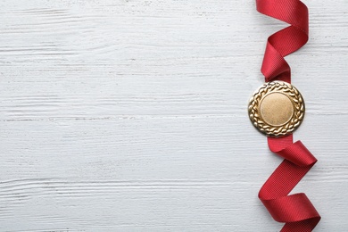 Gold medal with space for design on white wooden background, top view. Victory concept