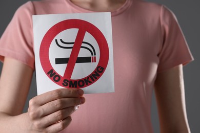 Photo of Woman holding card with no smoking sign on gray background, closeup