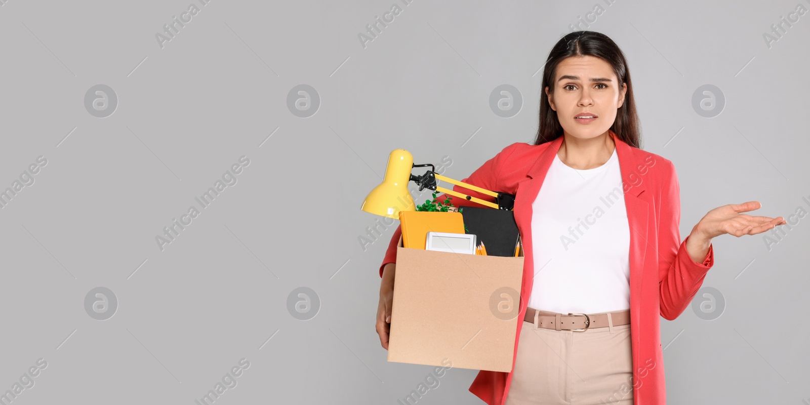 Photo of Unemployed woman with box of personal office belongings on grey background. Space for text