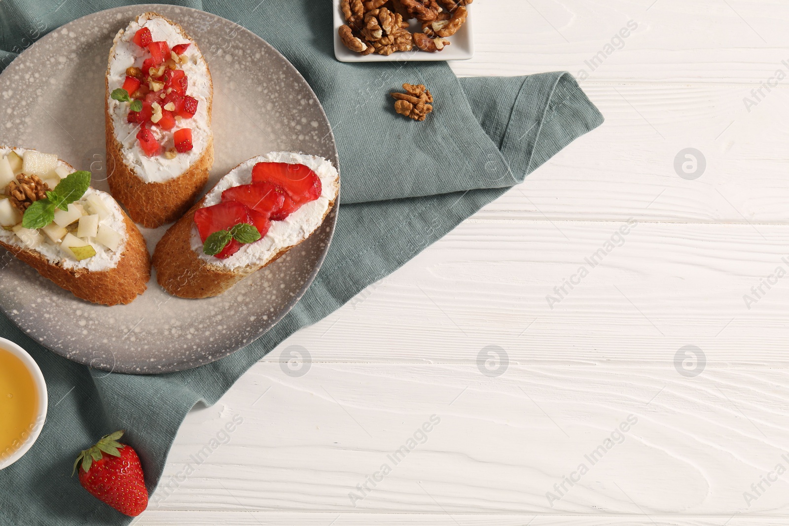 Photo of Delicious ricotta bruschettas with pear, strawberry and walnut on white wooden table, flat lay. Space for text