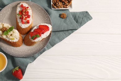 Photo of Delicious ricotta bruschettas with pear, strawberry and walnut on white wooden table, flat lay. Space for text