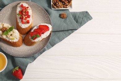 Delicious ricotta bruschettas with pear, strawberry and walnut on white wooden table, flat lay. Space for text