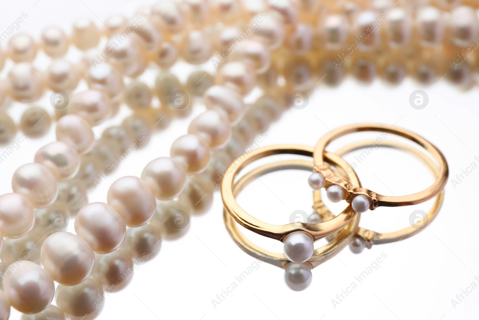 Photo of Elegant necklace and rings with pearls on mirror surface, closeup