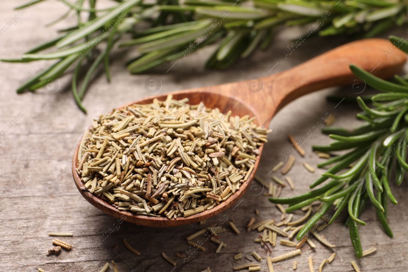 Photo of Spoon with dry and fresh rosemary on wooden table, closeup