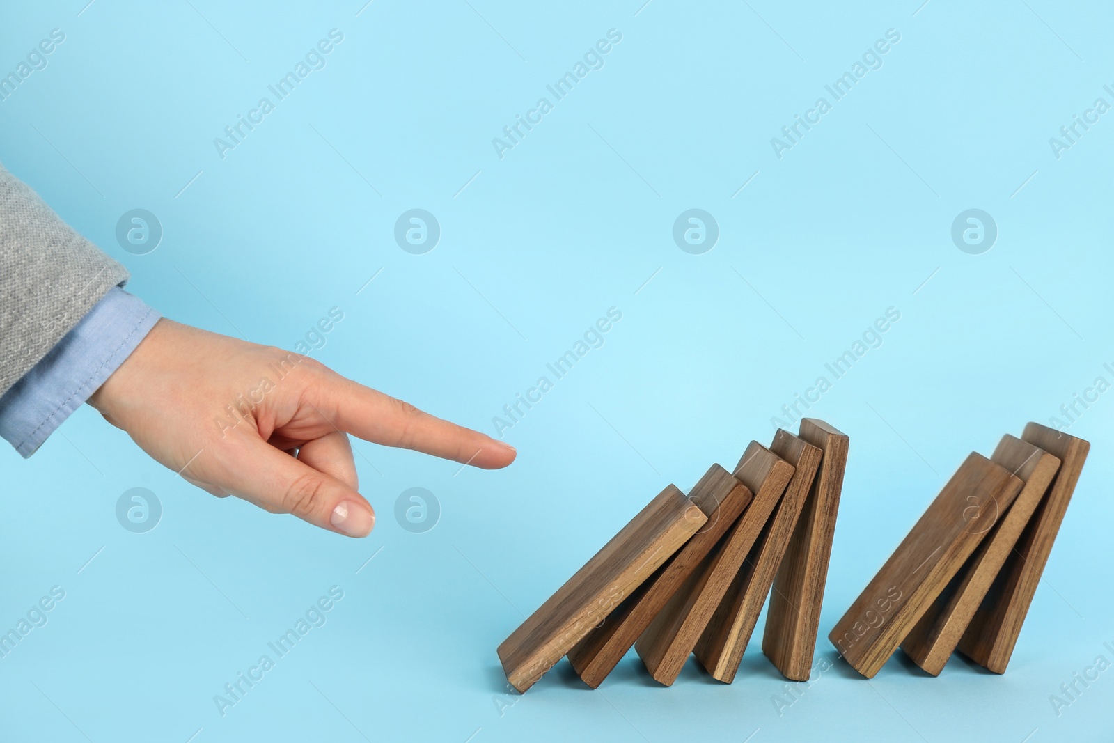 Photo of Woman causing chain reaction by pushing domino tile on light blue background, closeup