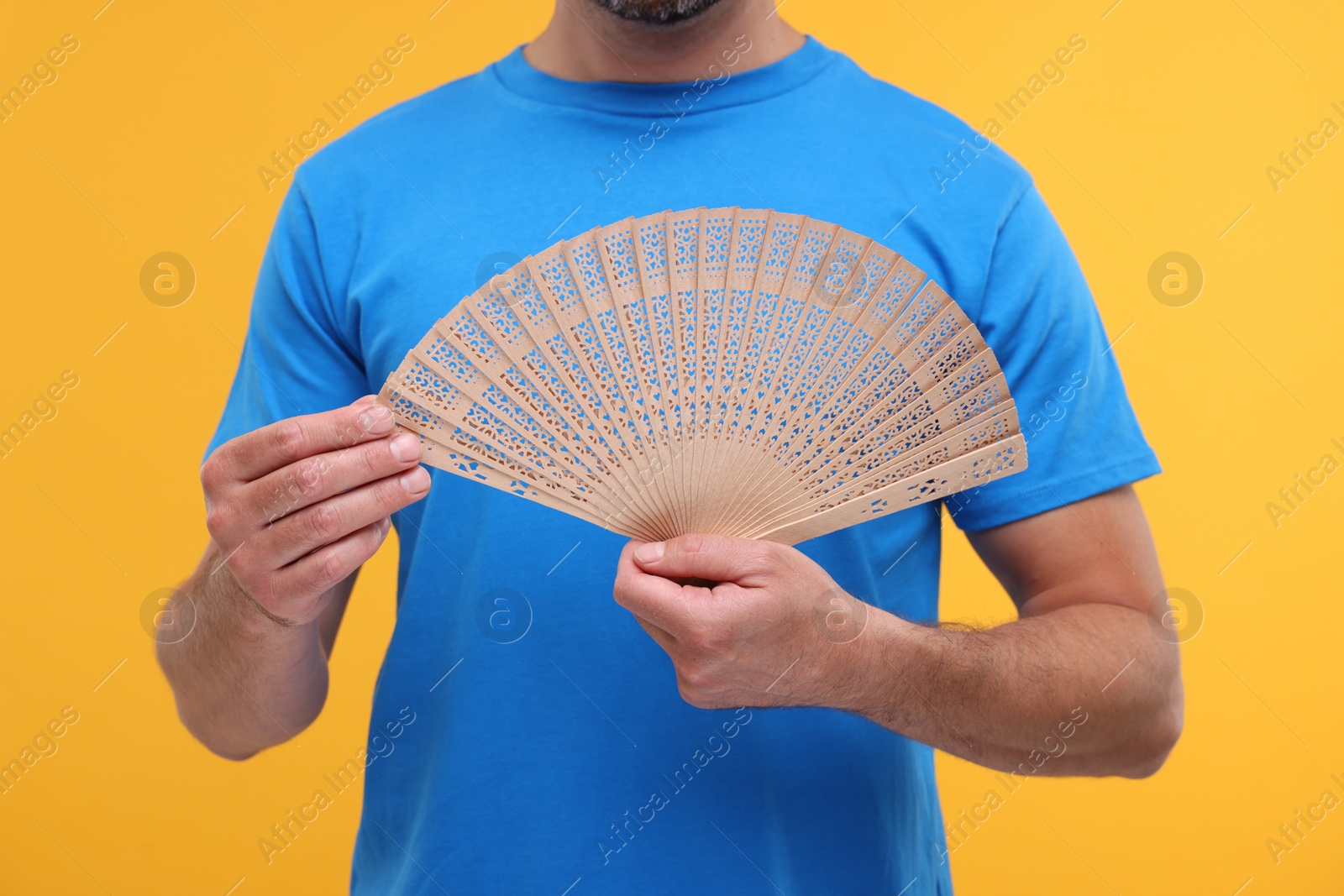 Photo of Man holding hand fan on orange background, closeup
