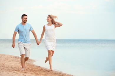 Happy romantic couple running together on beach, space for text