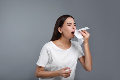 Young woman suffering from allergy on grey background