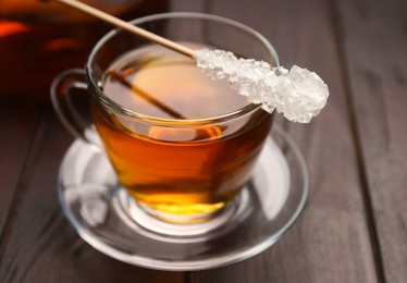 Photo of Stick with sugar crystals and cup of tea on wooden table, closeup