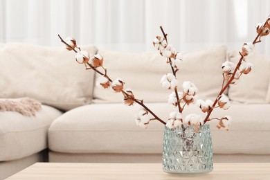 Photo of Cotton branches with fluffy flowers on wooden table in cozy room. Space for text