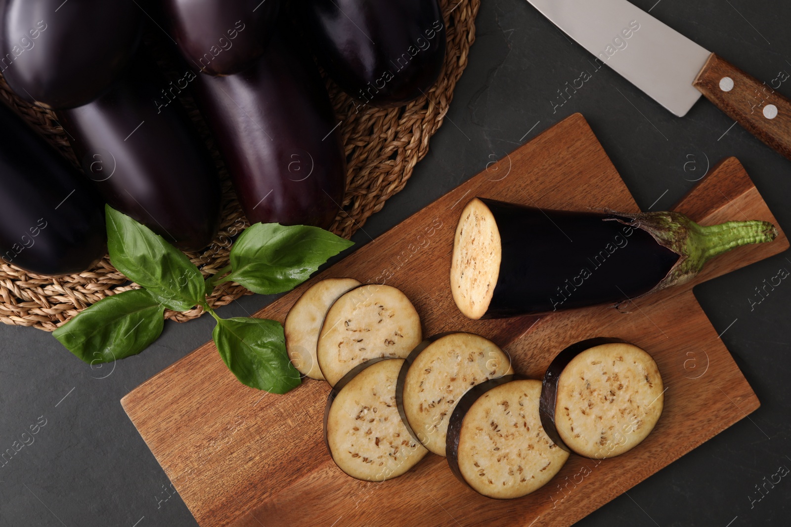 Photo of Cut and whole raw ripe eggplants on black table, flat lay
