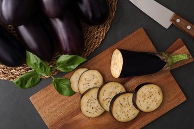 Cut and whole raw ripe eggplants on black table, flat lay