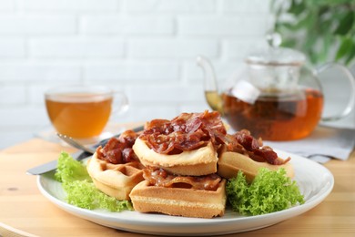 Photo of Tasty Belgian waffles served with bacon, lettuce and tea on wooden table, closeup