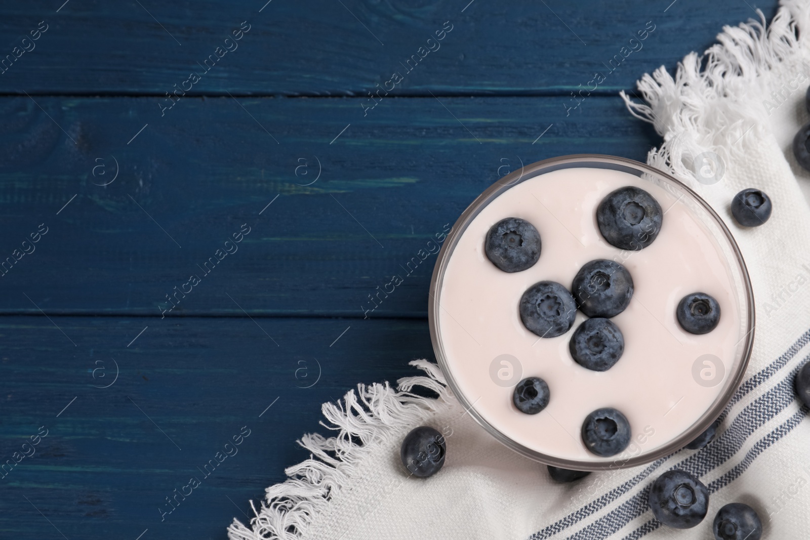 Photo of Tasty yogurt served with blueberries on blue wooden table, flat lay. Space for text