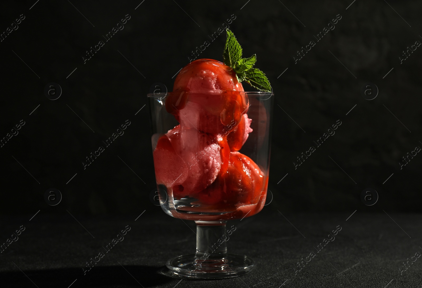 Photo of Delicious ice cream with sauce in dessert bowl on black table against dark background