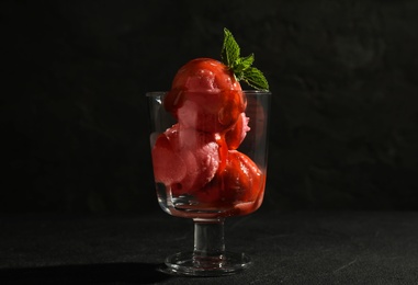 Delicious ice cream with sauce in dessert bowl on black table against dark background