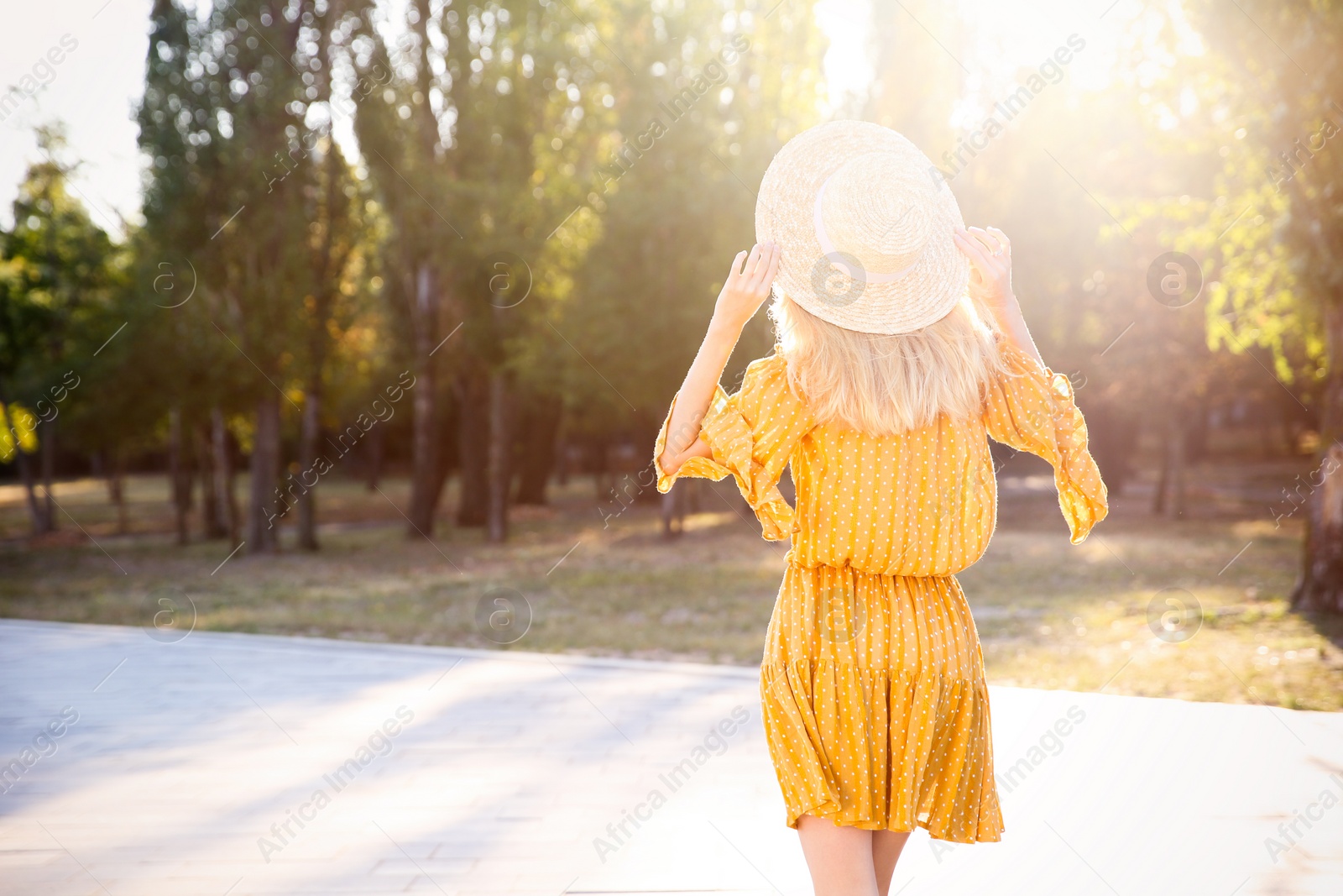 Photo of Woman in stylish yellow dress and straw hat outdoors, back view