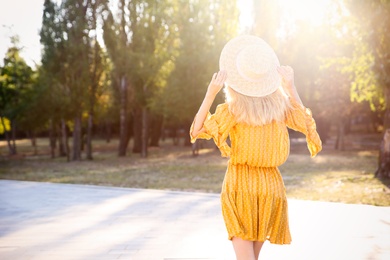 Photo of Woman in stylish yellow dress and straw hat outdoors, back view