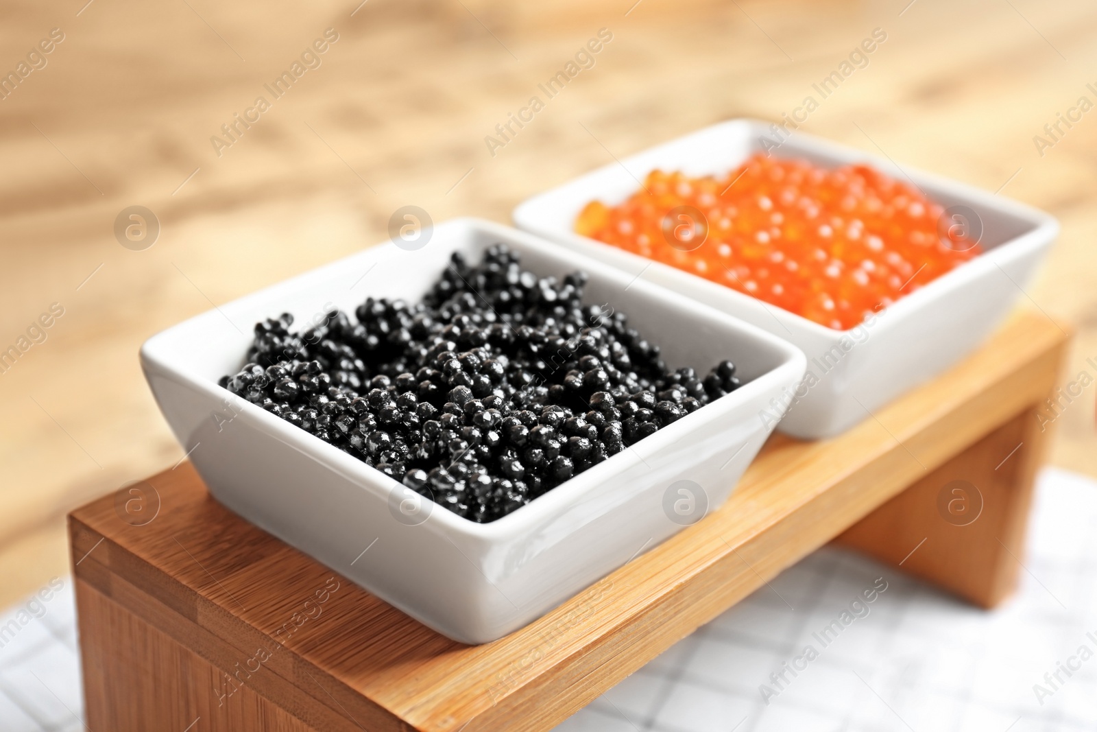 Photo of Bowls with black and red caviar on wooden stand