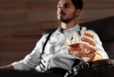 Man with glass of whiskey sitting in armchair, closeup. Space for text