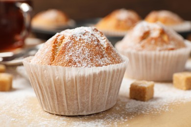 Photo of Tasty muffin powdered with sugar on table, closeup