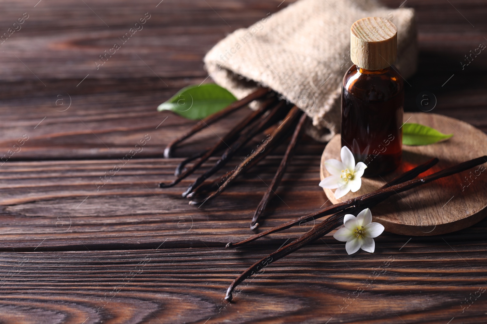 Photo of Vanilla pods, flowers, leaves and bottle with essential oil on wooden table, closeup. Space for text