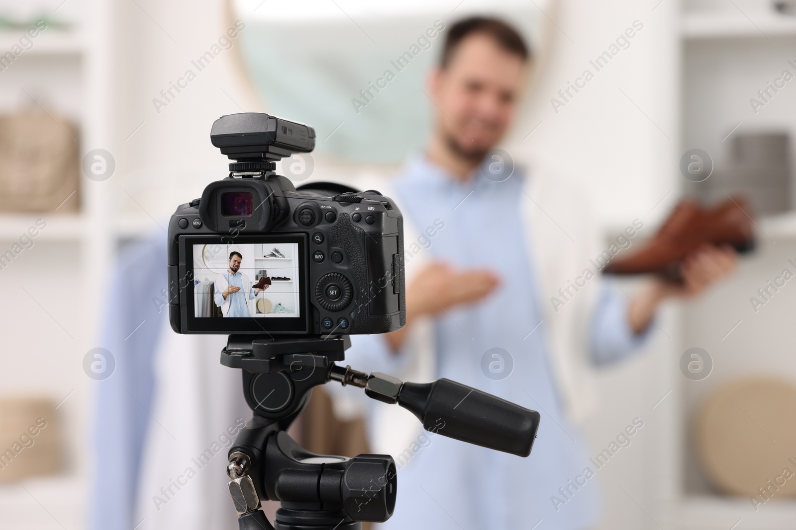 Photo of Fashion blogger showing shoe while recording video at home, focus on camera