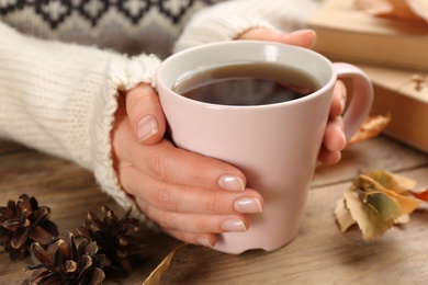 Woman with cup of hot drink at wooden table, closeup. Cozy autumn atmosphere