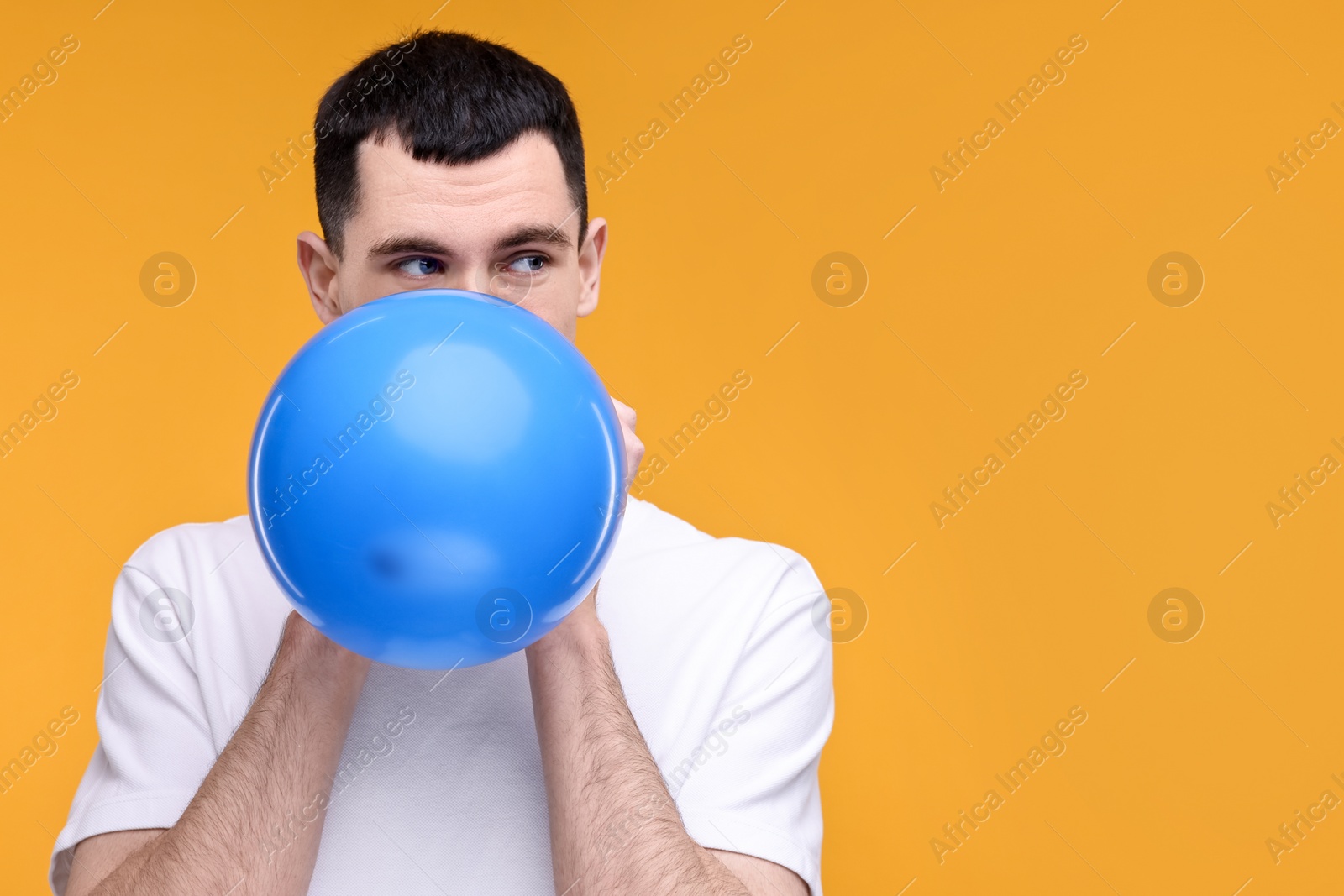 Photo of Young man inflating light blue balloon on yellow background. Space for text