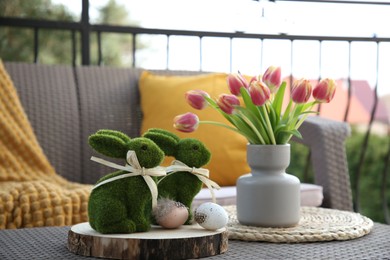 Terrace with Easter decorations. Bouquet of tulips in vase, bunny figures and decorative eggs on table outdoors