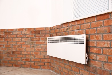 Modern heating convector on brick wall indoors