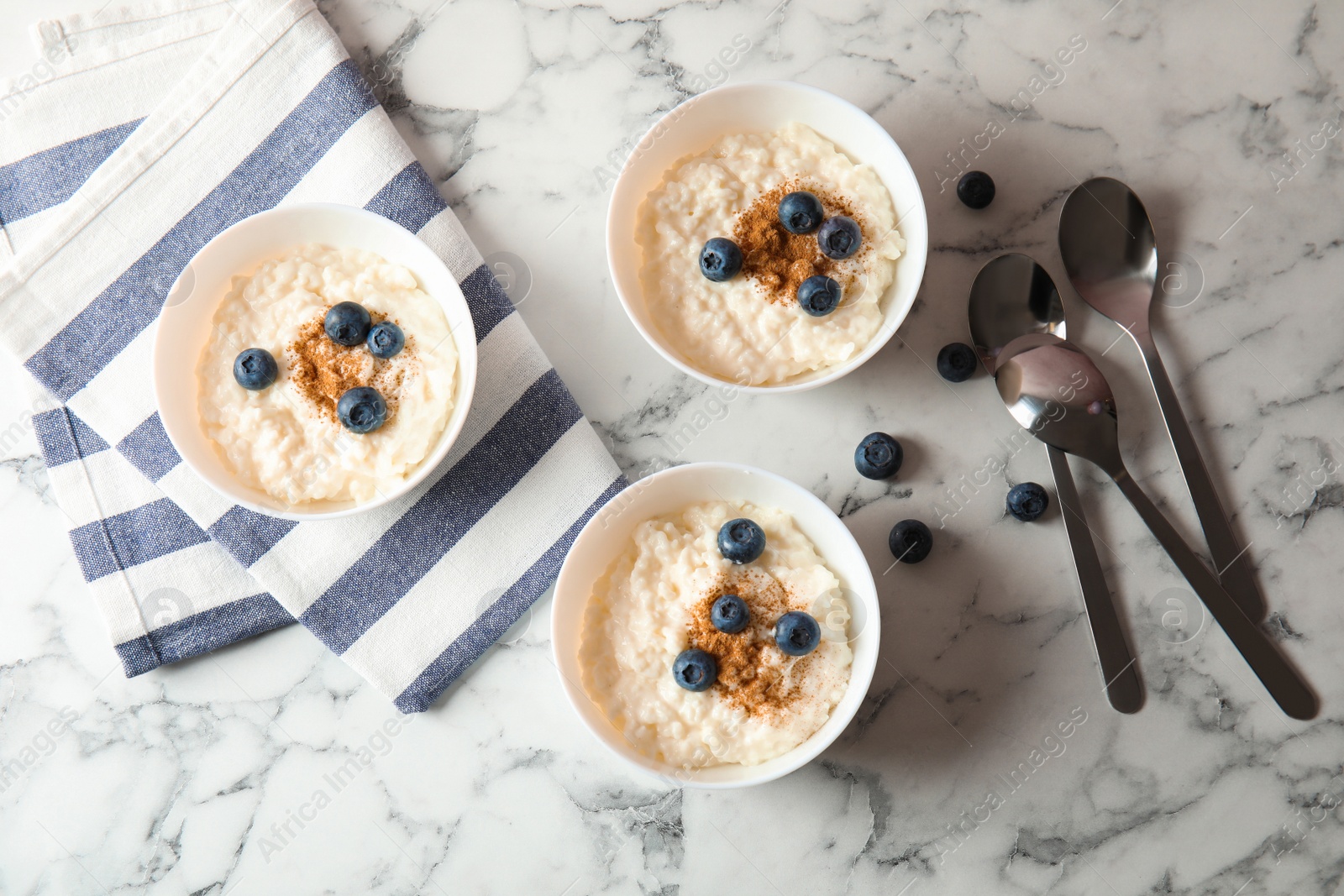 Photo of Creamy rice pudding with cinnamon and blueberries in bowls served on marble table, top view