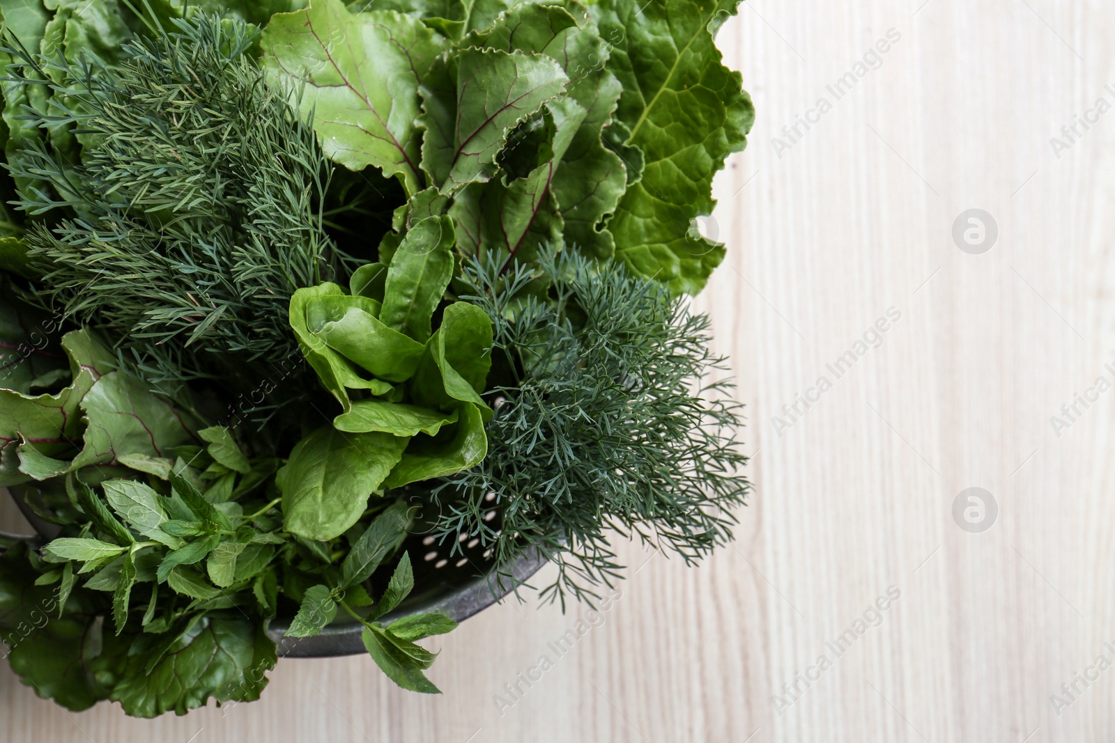 Photo of Different herbs in colander on white wooden table, space for text