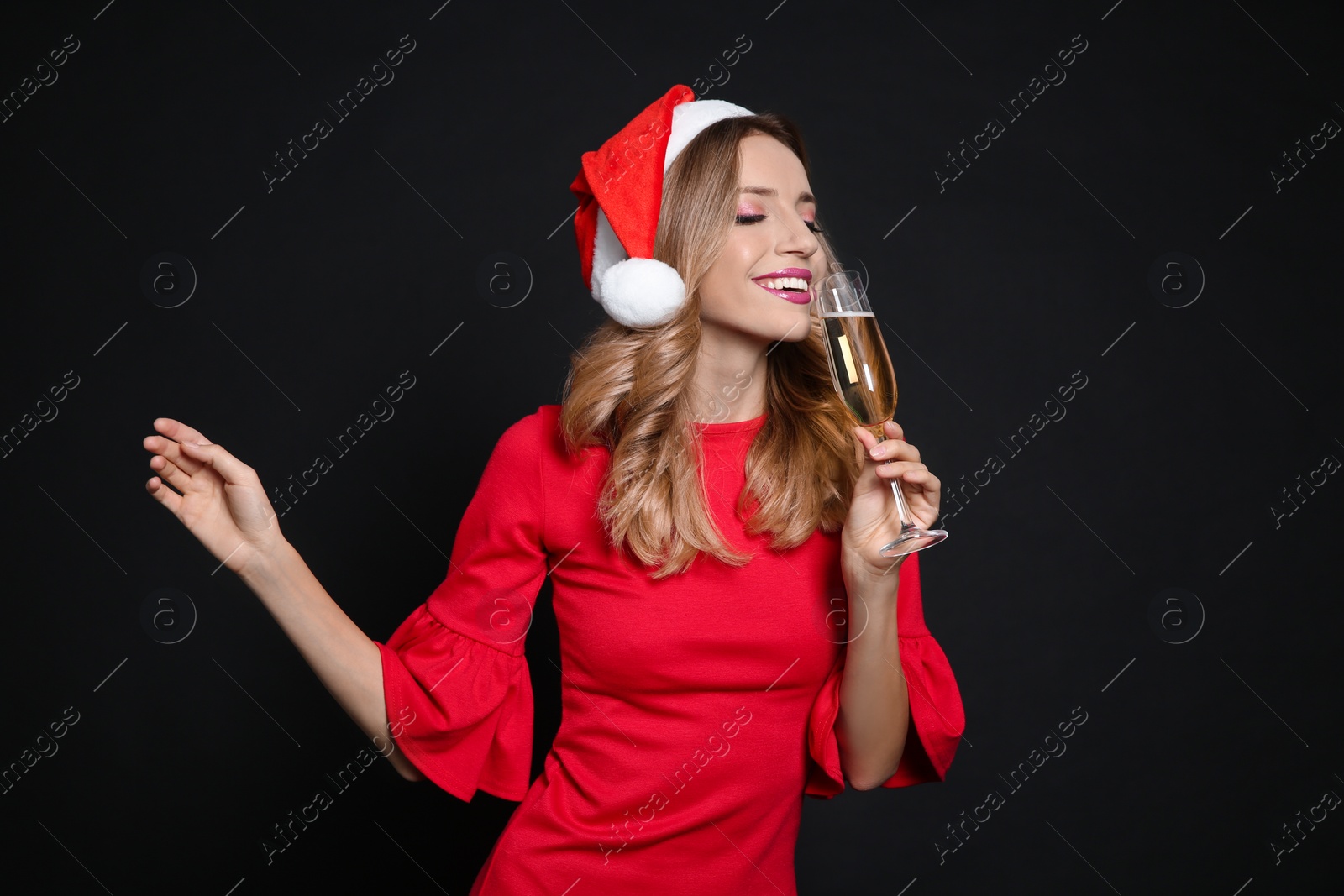 Photo of Happy woman in Santa hat with glass of champagne on black background. Christmas party