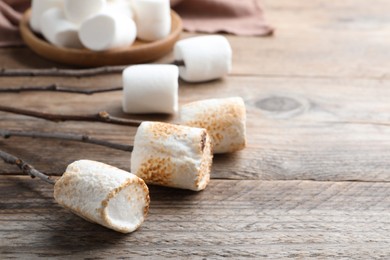 Photo of Sticks with roasted marshmallows on wooden table, closeup. Space for text