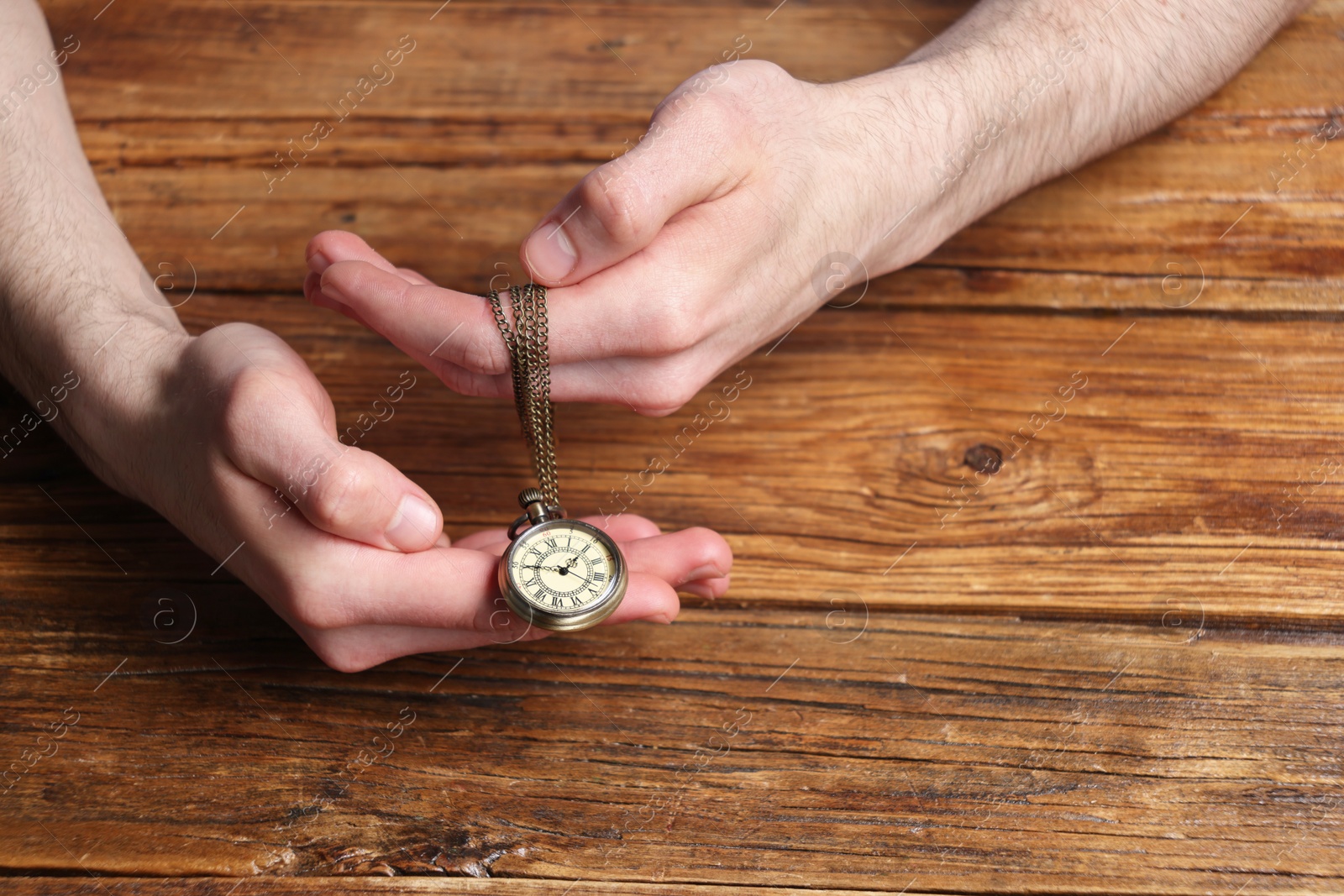 Photo of Man holding chain with elegant pocket watch at wooden table, closeup. Space for text