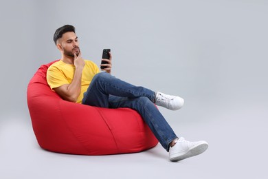 Photo of Young man using smartphone on bean bag chair against grey background