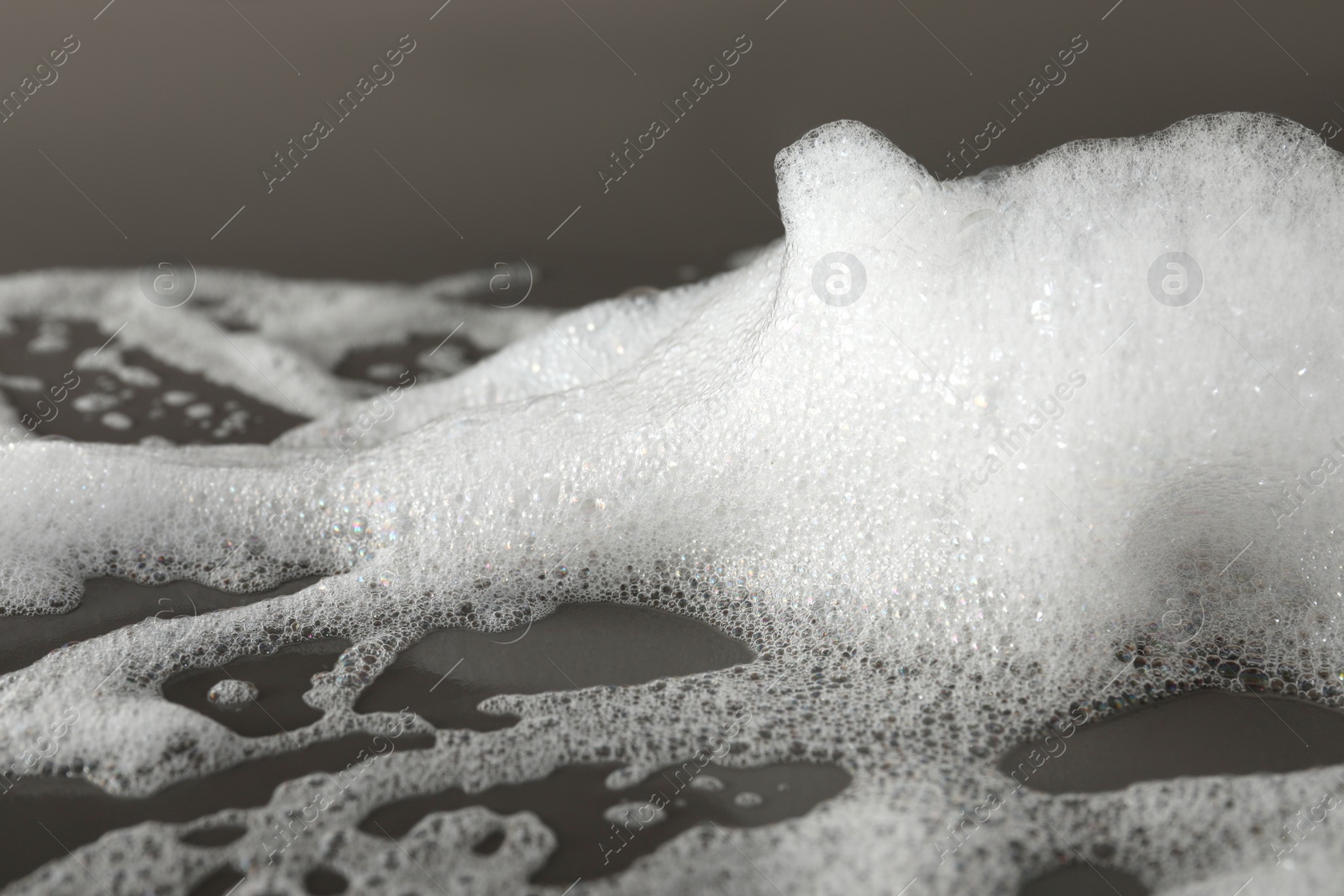 Photo of Fluffy bath foam on grey background, closeup