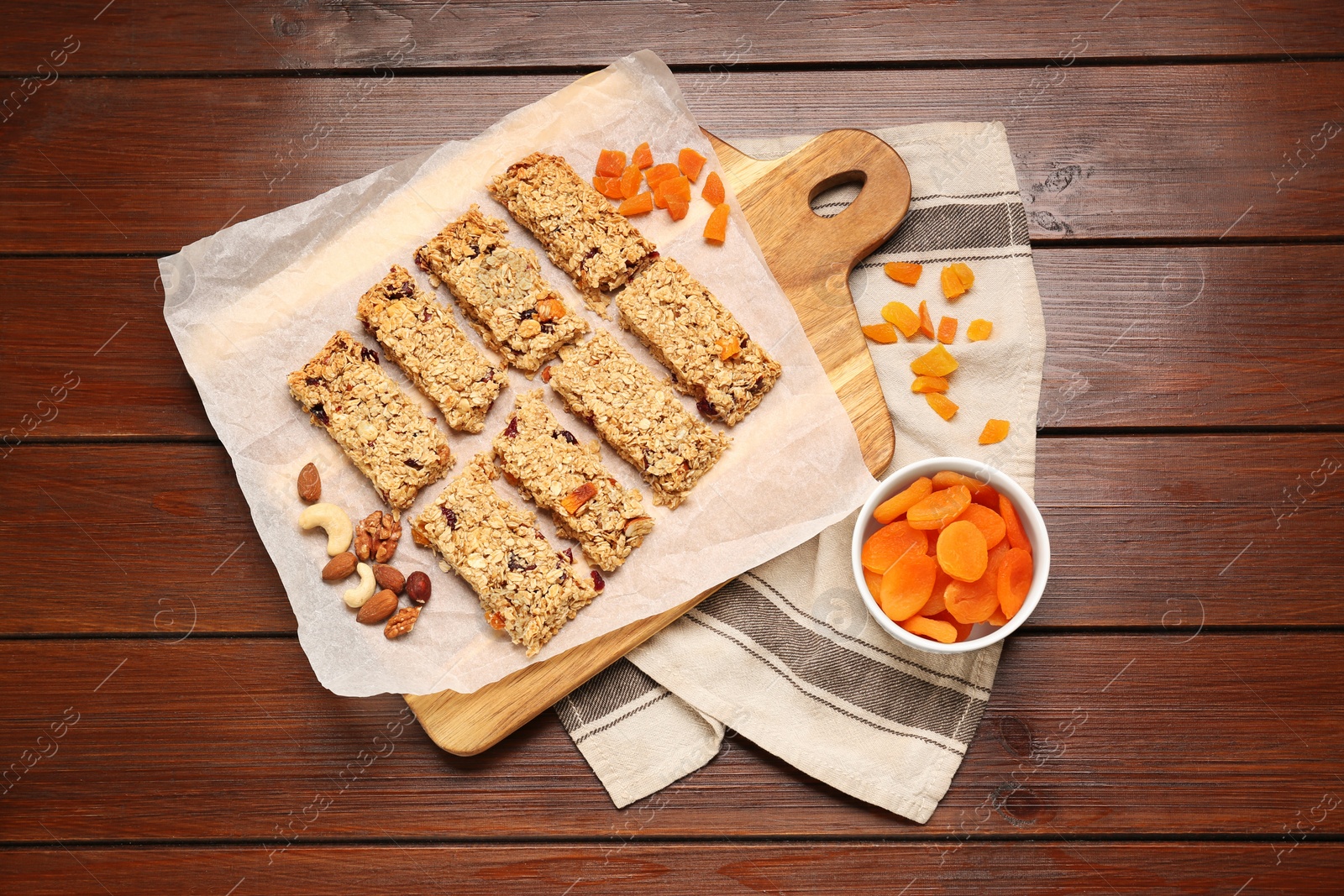 Photo of Tasty granola bars, dried apricots and nuts on wooden table, flat lay