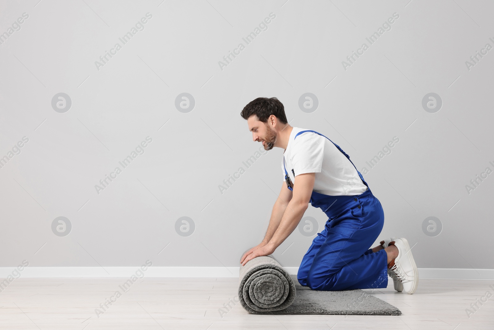 Photo of Worker unrolling new carpet on floor in room, space for text